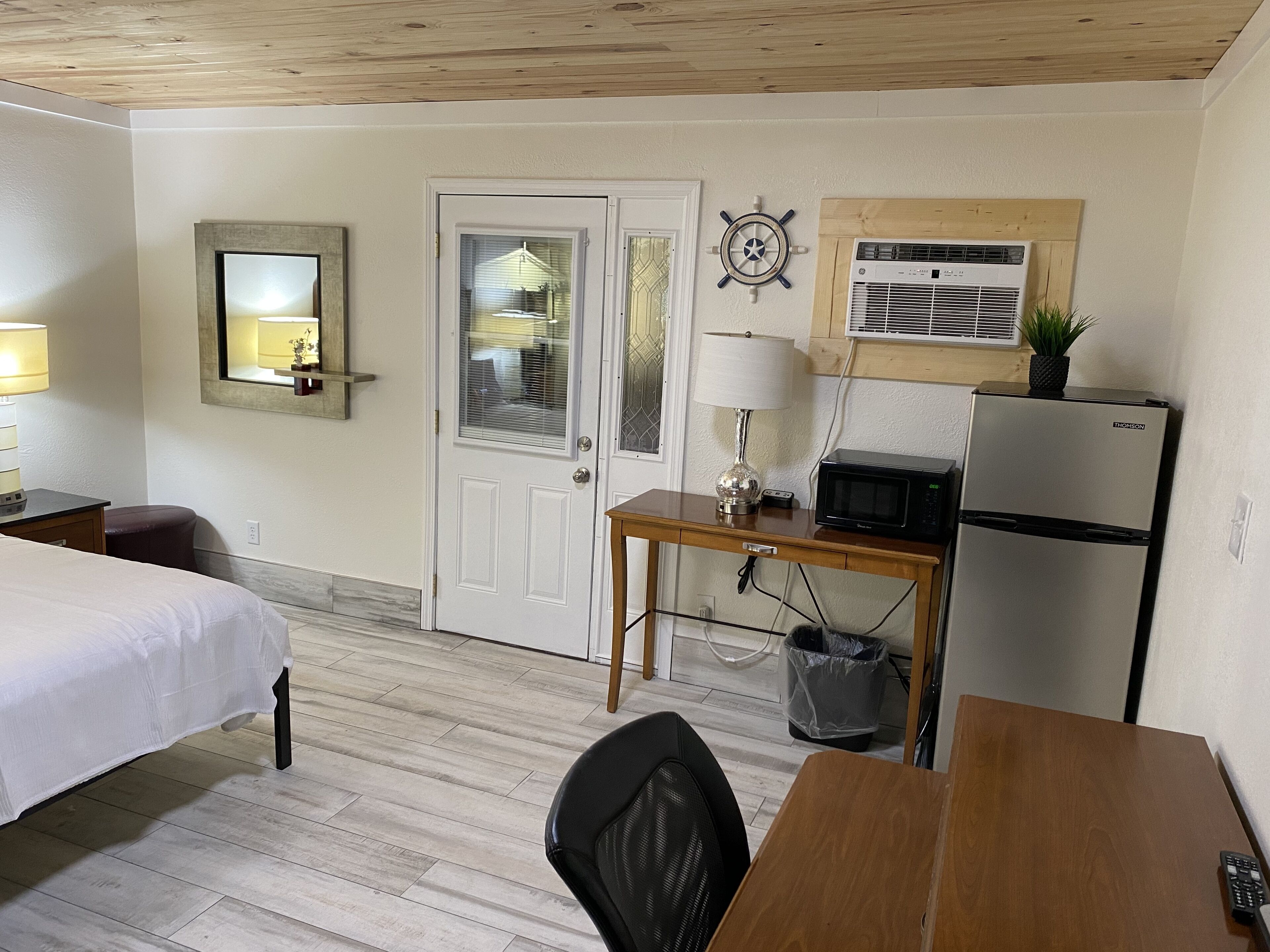 Hotelkamer met twee bedden, een houten bureau, een stoel, een magnetron, een koelkast, een prullenbak, een lamp, een spiegel en een wandgemonteerde airconditioner.