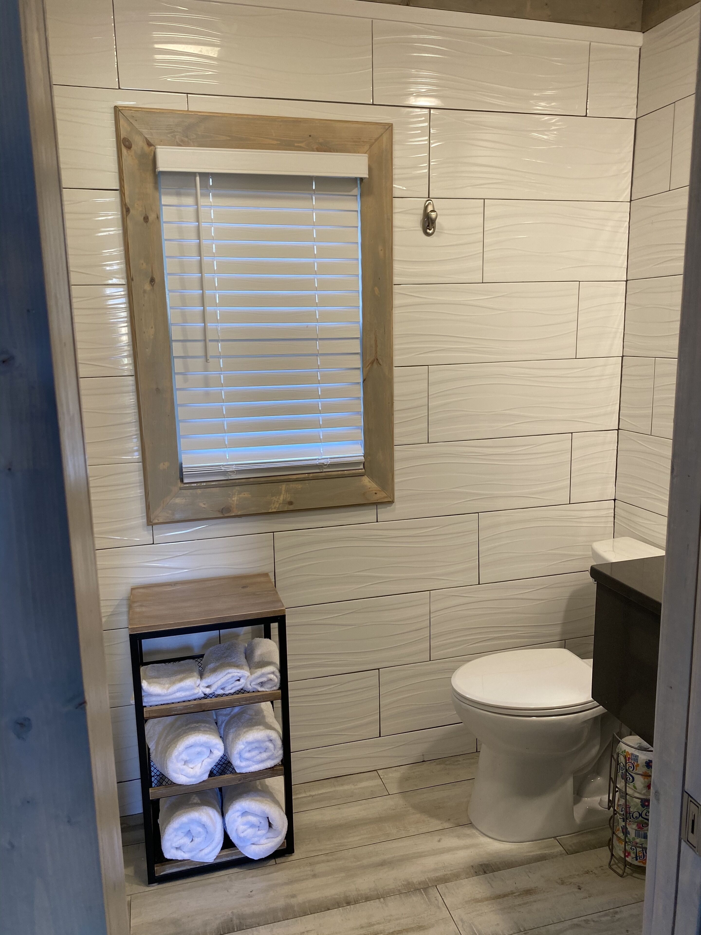 A bathroom with a wooden vanity, a toilet, and a shelf with towels.