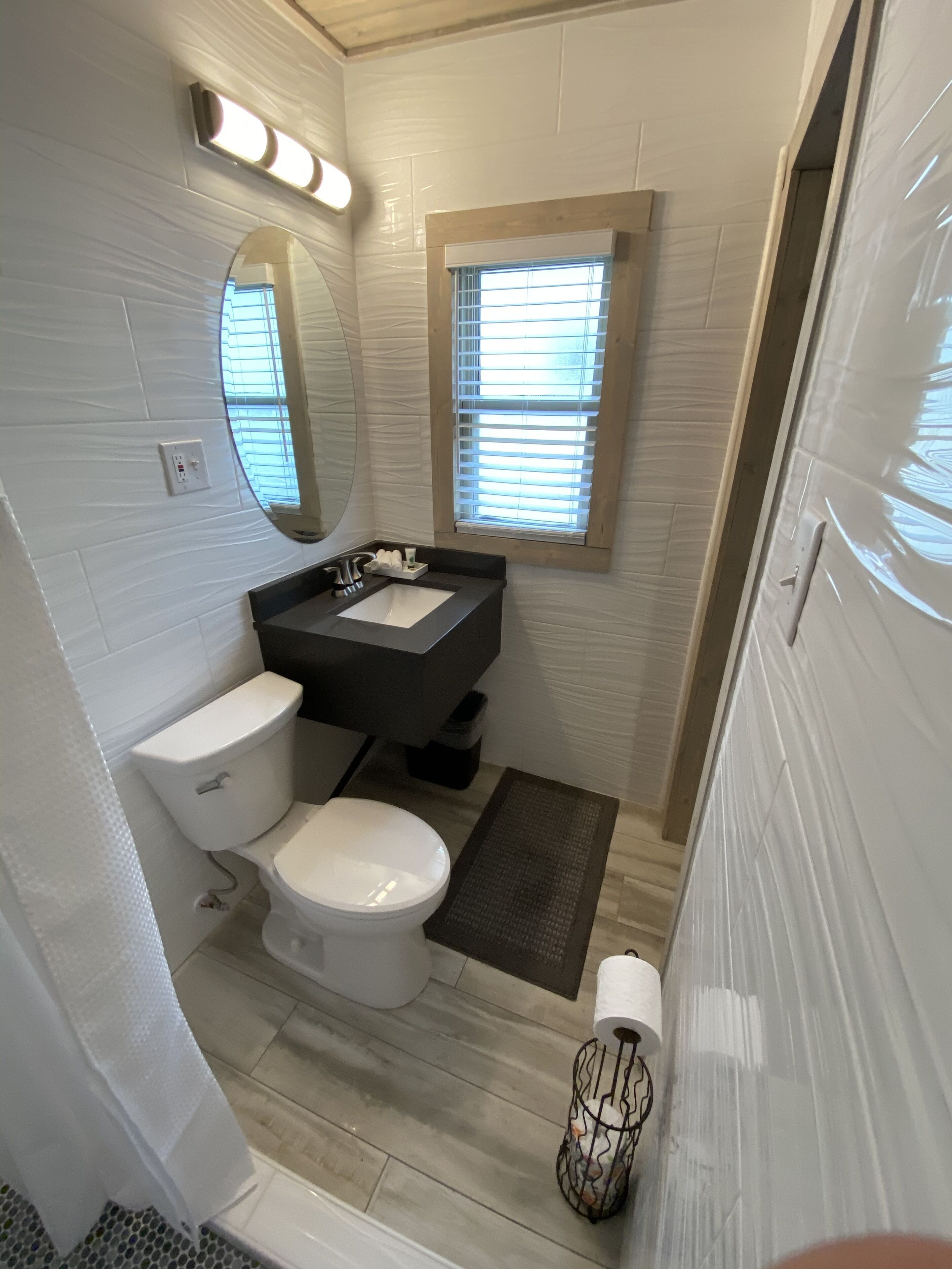 A bathroom with a toilet, sink, mirror, and window.