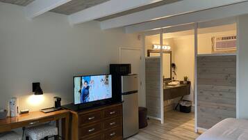 Hotellihuone, jossa on puinen työpöytä, televisio, sänky sekä kylpyhuone, jossa on puinen pesuallas ja peili.