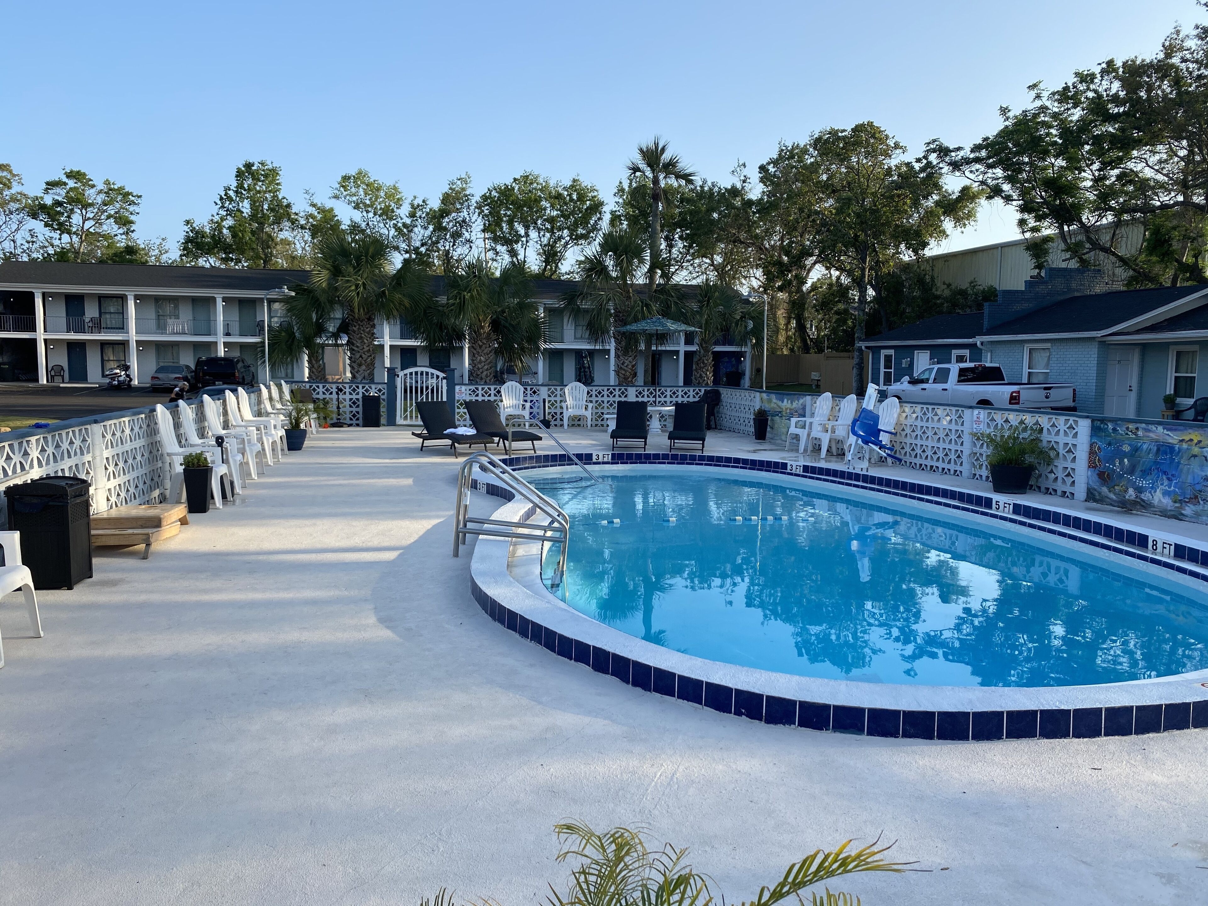 A swimming pool with a tiled edge, surrounded by lounge chairs and a fence.