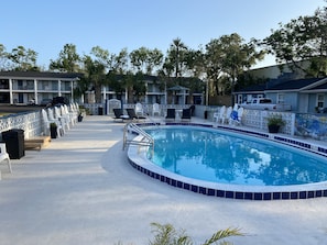 A swimming pool with a tiled edge, surrounded by lounge chairs and a fence.