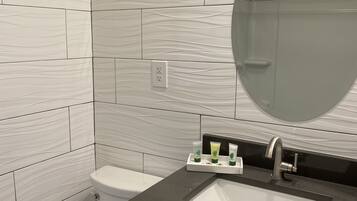 Un baño con baldosas de mármol blanco, un lavabo negro, un espejo y artículos de tocador.