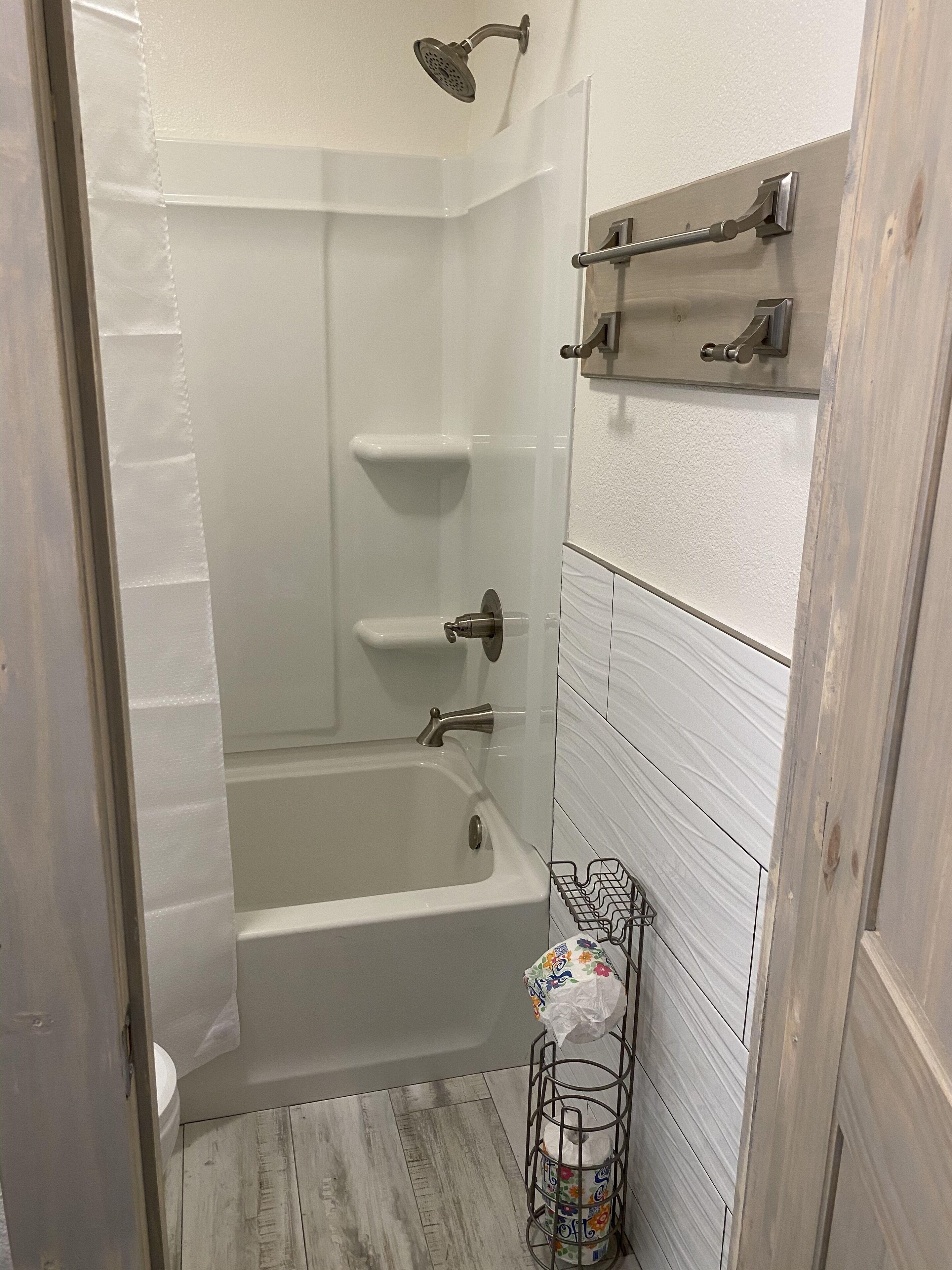 Een badkamer met een witte badkuip, douchekop en toilet. Daarboven een plankje en aan de muur een handdoekhouder.