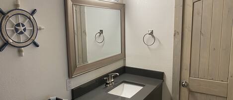 Une salle de bain avec un lavabo noir, un miroir, un élément décoratif en forme de roue de navire et une porte en bois.