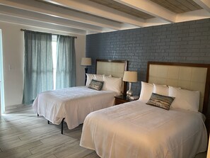 Habitación de hotel con dos camas, un muro decorativo de ladrillo y techo de madera.