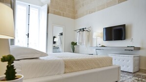 A modern bedroom with a large bed, a flat-screen TV, a vanity with a mirror, and a hanging towel rack. - Le Dimore dell'Acqua (Matera)