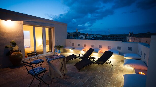 A rooftop terrace with a dining area, lounge chairs, and a view of the cityscape at dusk. - Le Dimore dell'Acqua (Matera)