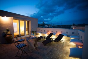 A rooftop terrace with a dining area, lounge chairs, and a view of the cityscape at dusk. - Le Dimore dell'Acqua (Matera)
