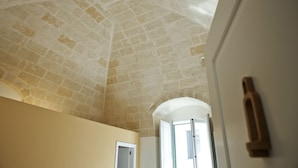 A room with a high, vaulted ceiling made of stone tiles, a white door, and a window with a view of the outside. - Le Dimore dell'Acqua (Matera)