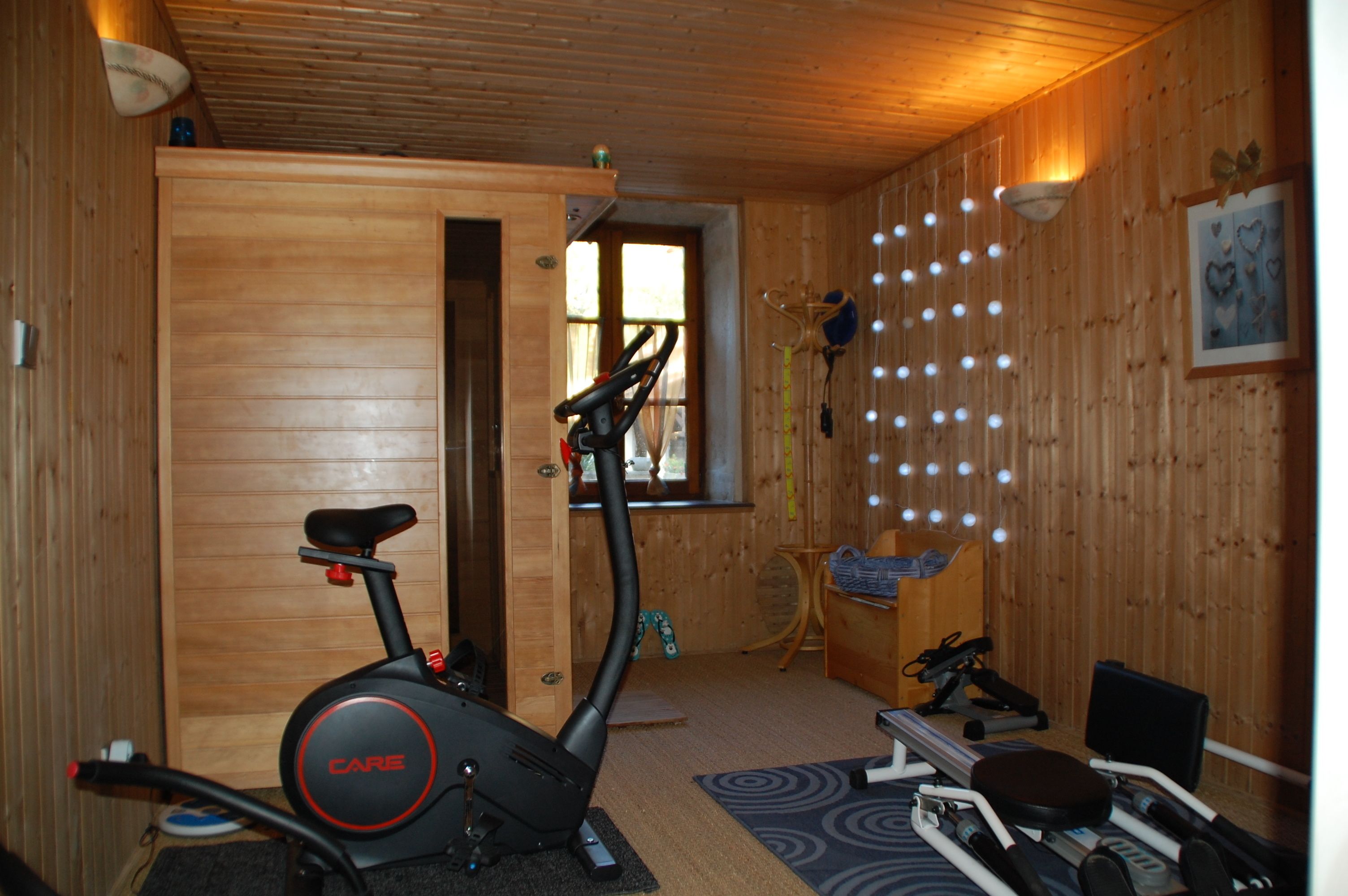 A room with a stationary bike, a treadmill, and a small table with a chair.