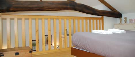 Un dormitorio con cabecera de listones de madera, una cama con colchón blanco y una mesita de noche de madera.