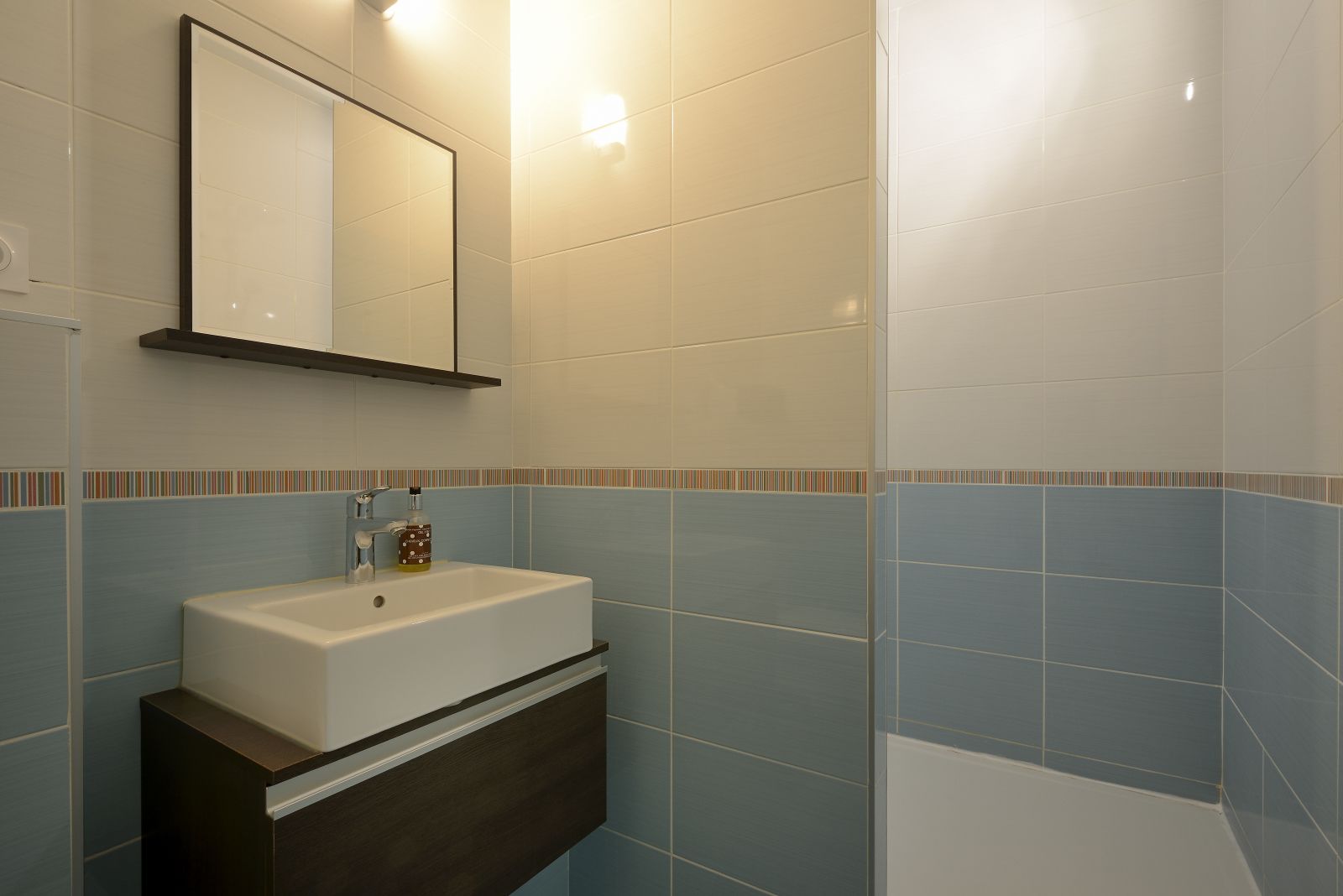 A bathroom with a white sink, a mirror, and a shower area.