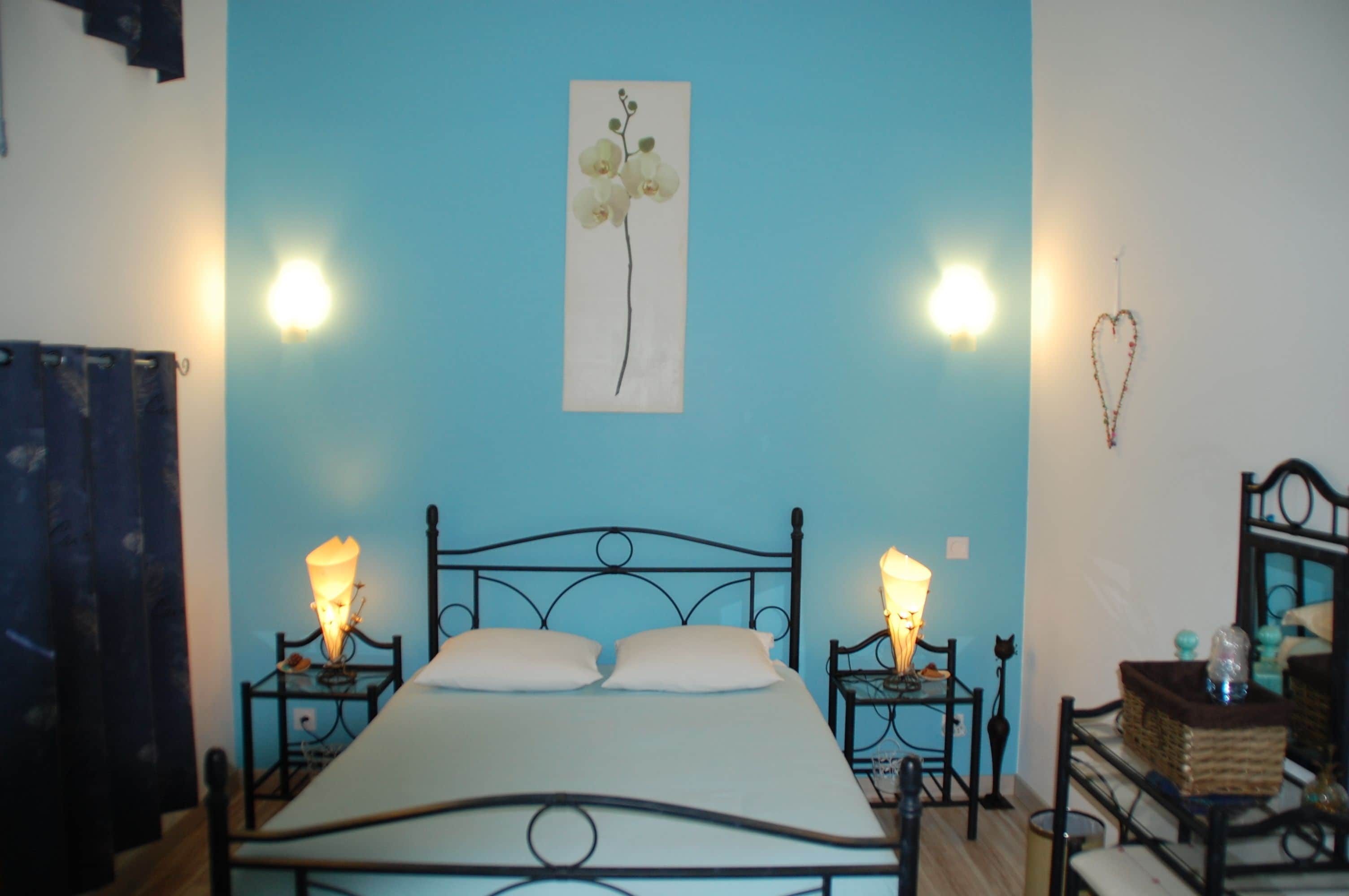 Een slaapkamer met een bed, twee nachtkastjes, een wandlamp en een hartvormige decoratie.
