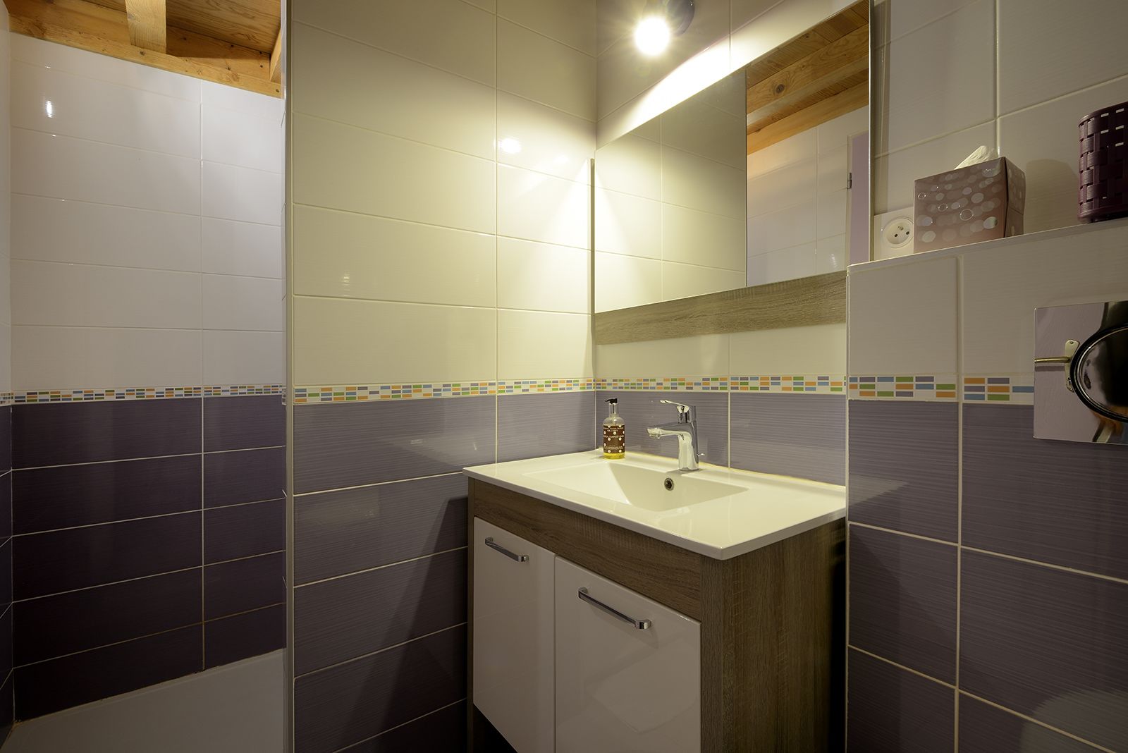 Un baño con lavamanos blanco, espejo y mueble de madera.