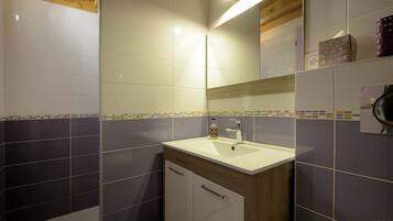 Un baño con lavamanos blanco, espejo y mueble de madera.