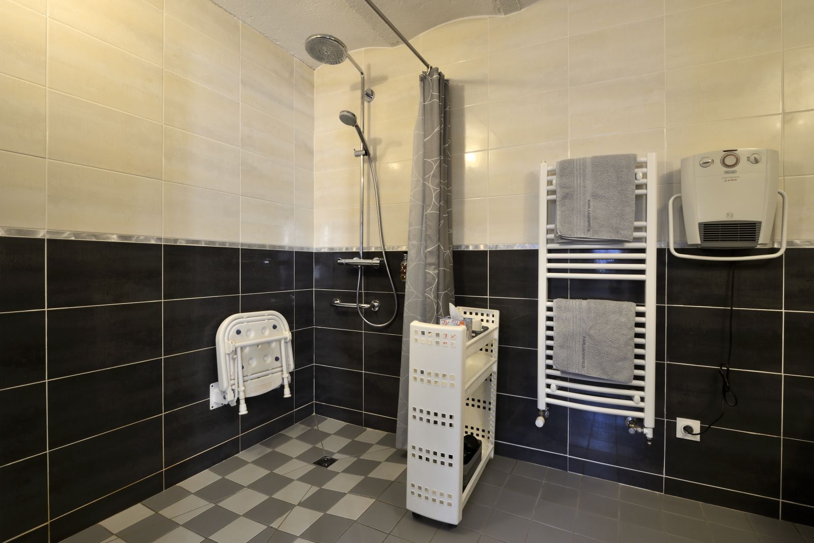 A bathroom with black and white tiles, a shower, a towel rack, and a hand dryer.
