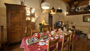 Un comedor con una mesa de madera dispuesta para una comida, un televisor al fondo y un armario de madera.