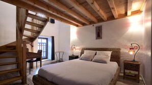 Un dormitorio con una cama grande, vigas de madera en el techo, una escalera y una pequeña mesa con lámpara.