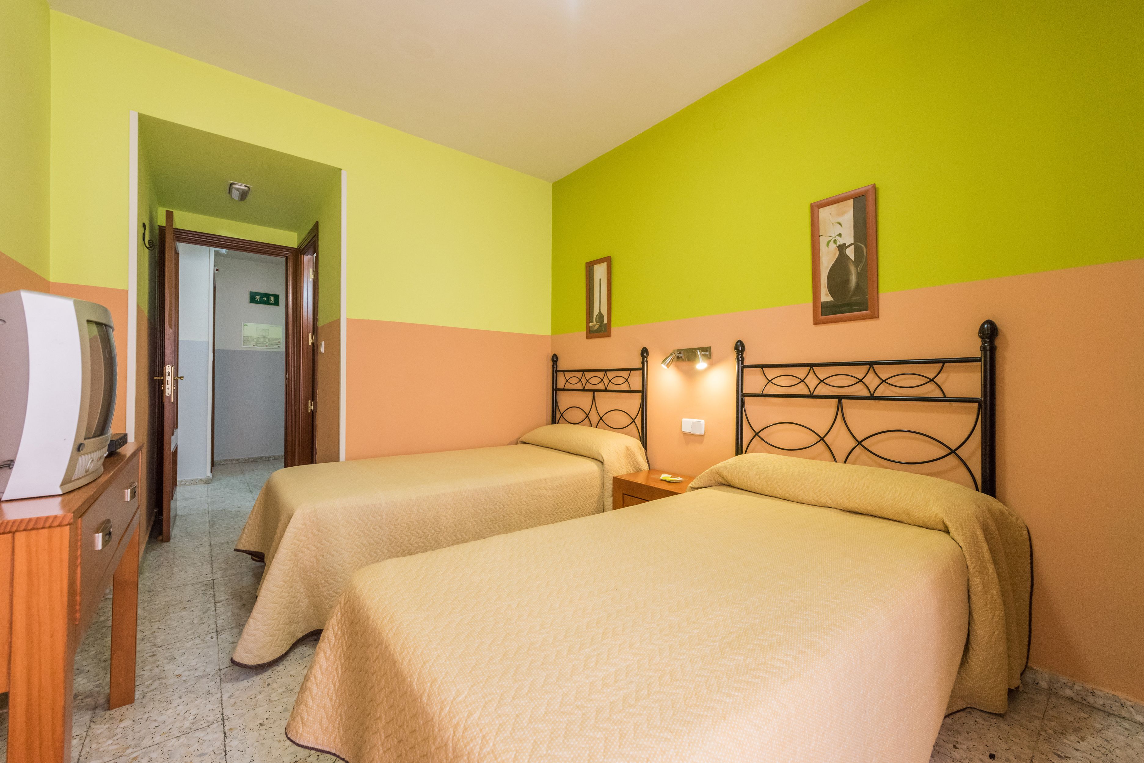 Habitación de hotel con dos camas, un aparador de madera, un televisor y una puerta que da a otra habitación.