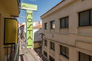A narrow street with a hostel sign and a building with multiple windows. - Hostal Arkanta (Arganda del Rey)