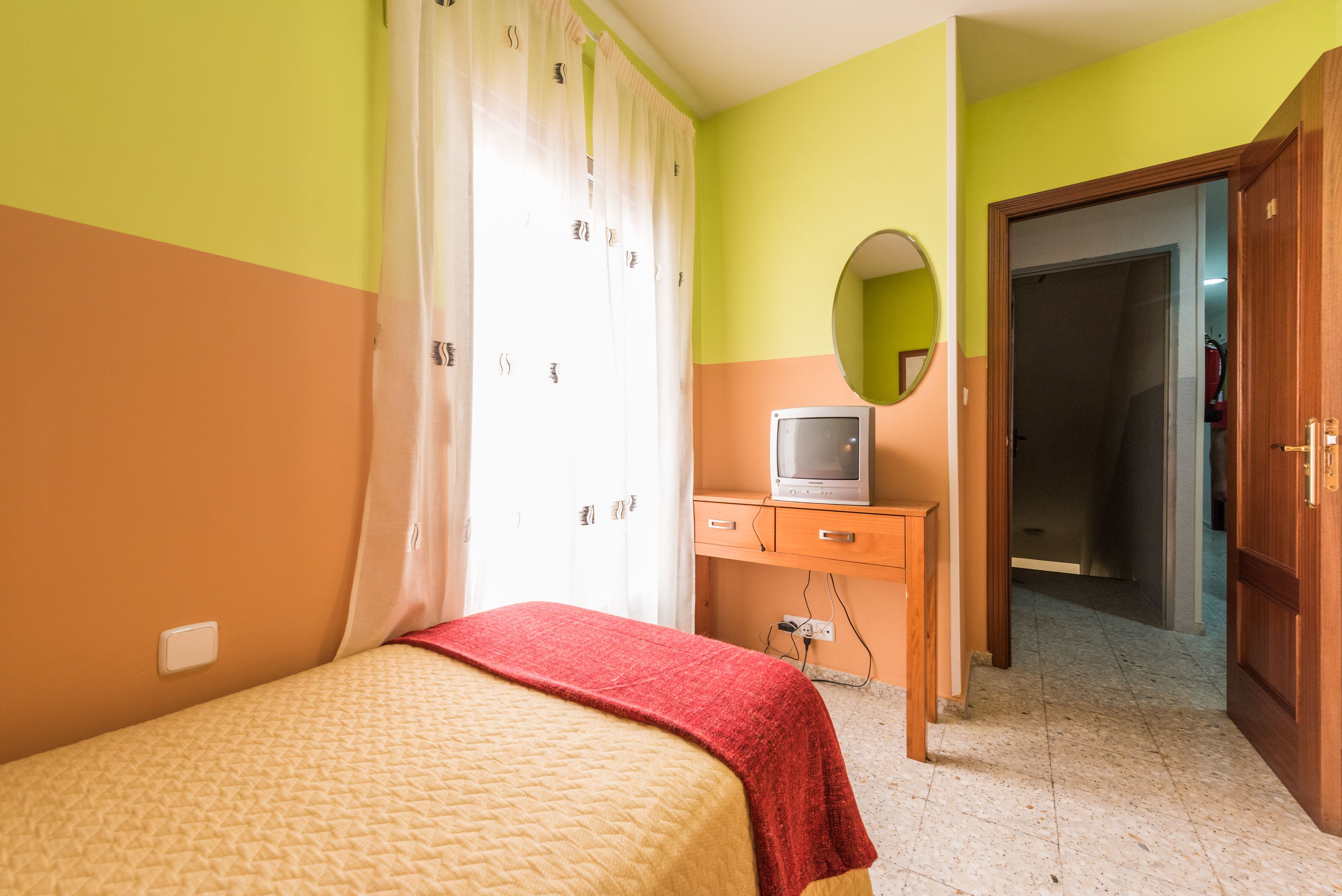 A bedroom with a bed, a television, a mirror, and a wardrobe.
