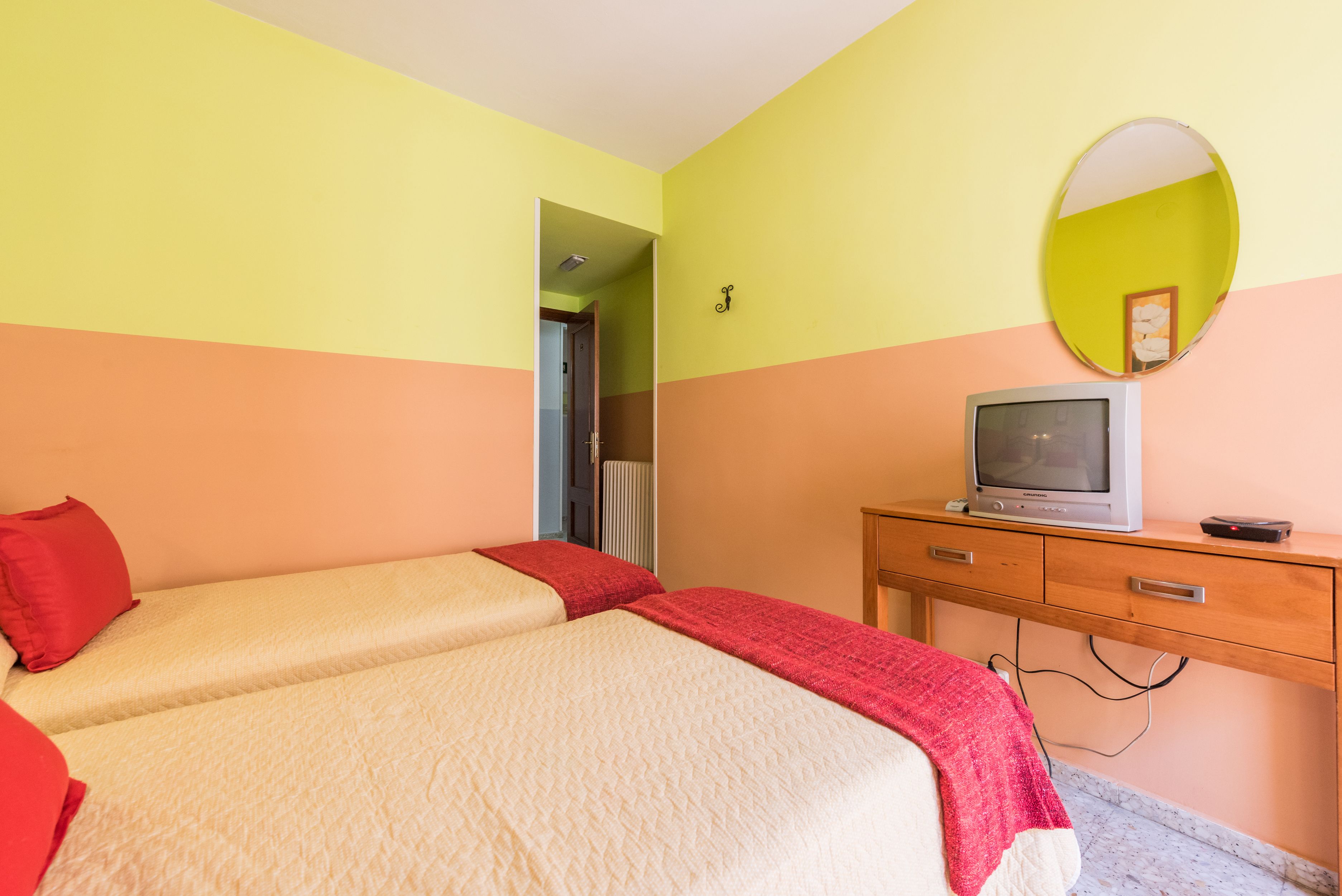 A room with two beds, a television, a mirror, and a wooden dresser.