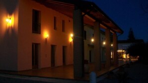 A building with multiple windows and a covered porch area, illuminated by exterior lights.