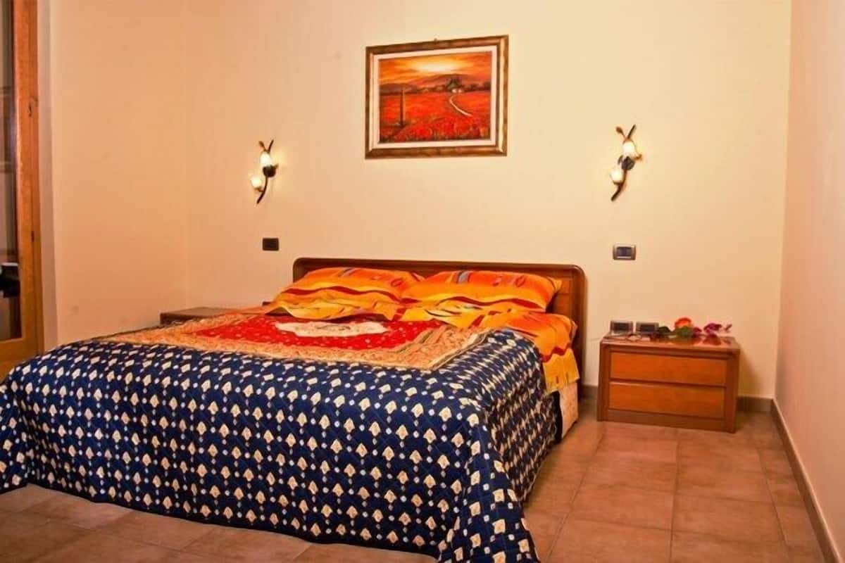 Een slaapkamer met een bed, nachtkastje, een wandlamp en een lijst met een schilderij.