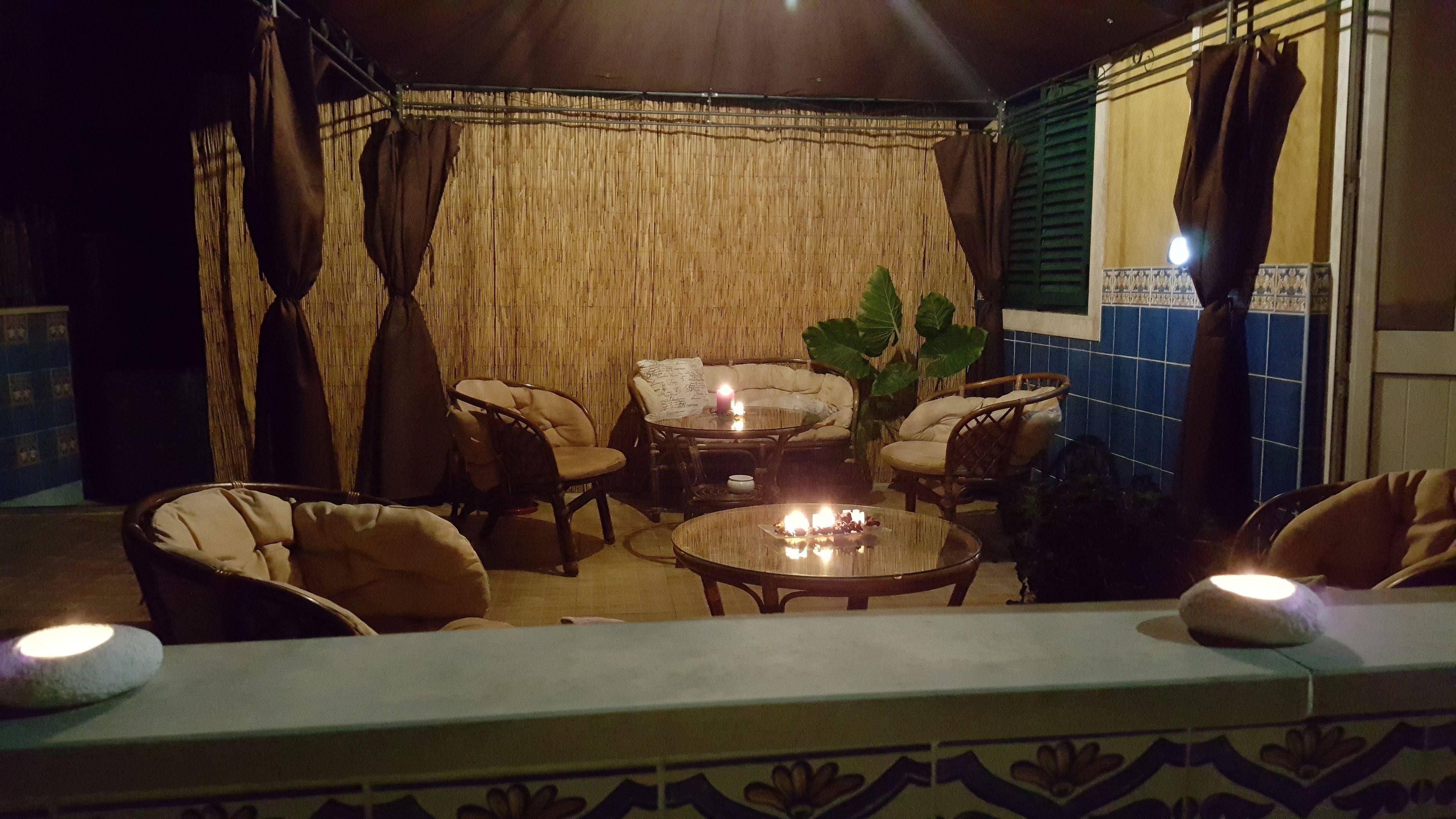 Un área de estar al aire libre acogedora con mobiliario de mimbre, una mesa redonda con velas y un fondo de techo de paja.