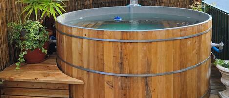 A wooden hot tub with steps leading up to it, surrounded by potted plants and a bamboo fence.