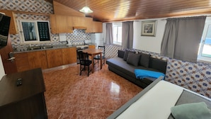 A compact kitchen with wooden cabinets, a dining area with a table and chairs, a sofa with cushions, and a patterned backsplash. - Guesthouse of Alcobaça (Alcobaça)