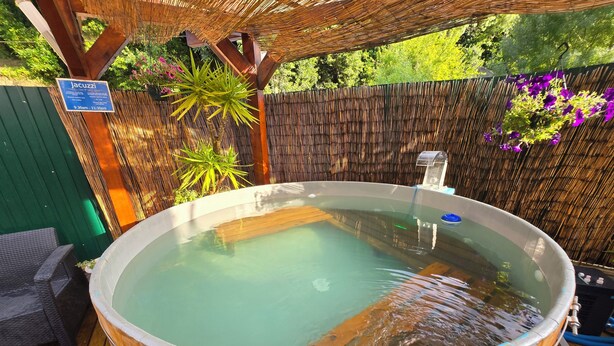 A wooden hot tub with a bamboo backdrop, surrounded by greenery and a sign indicating operating hours. - Guesthouse of Alcobaça (Alcobaça)