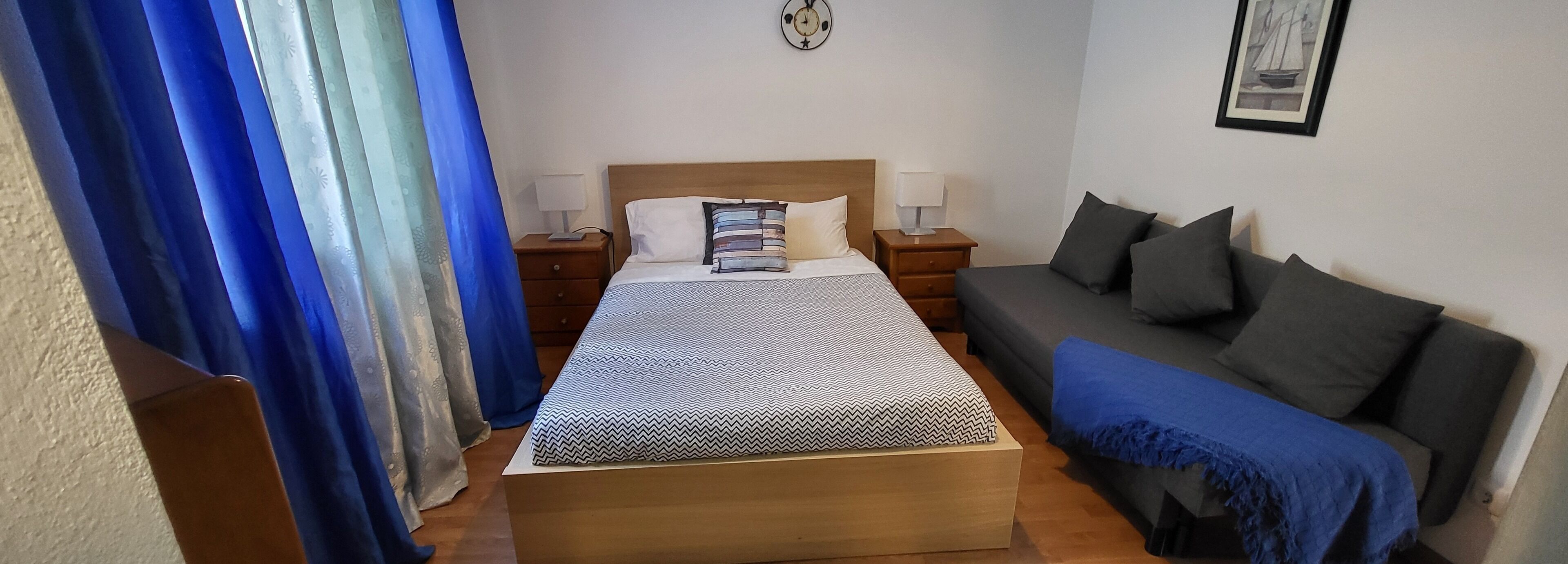 A bedroom with a bed, bedside tables, a nightstand, a sofa, and a wall clock.
