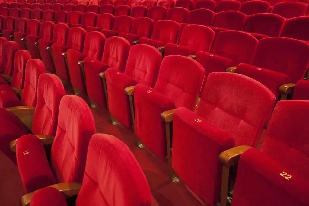 Rijen rode theaterstoelen met houten armleuningen.