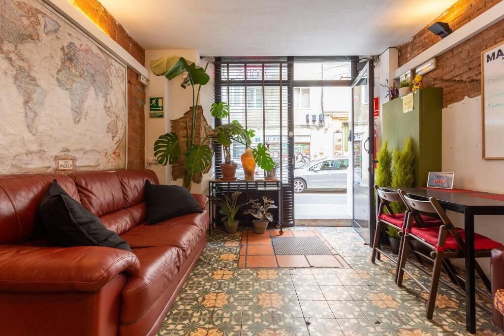 A cozy room with a leather sofa, a small table with chairs, a world map on the wall, and potted plants.