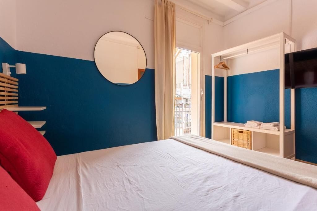 A hotel room with a bed, a mirror, a wardrobe, and a window with curtains.