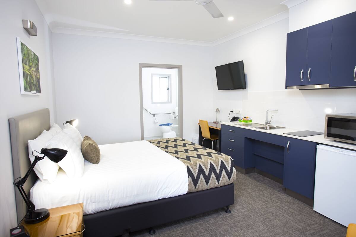 Ein modernes Hotelzimmer mit Bett, Schreibtisch und Küchenzeile.