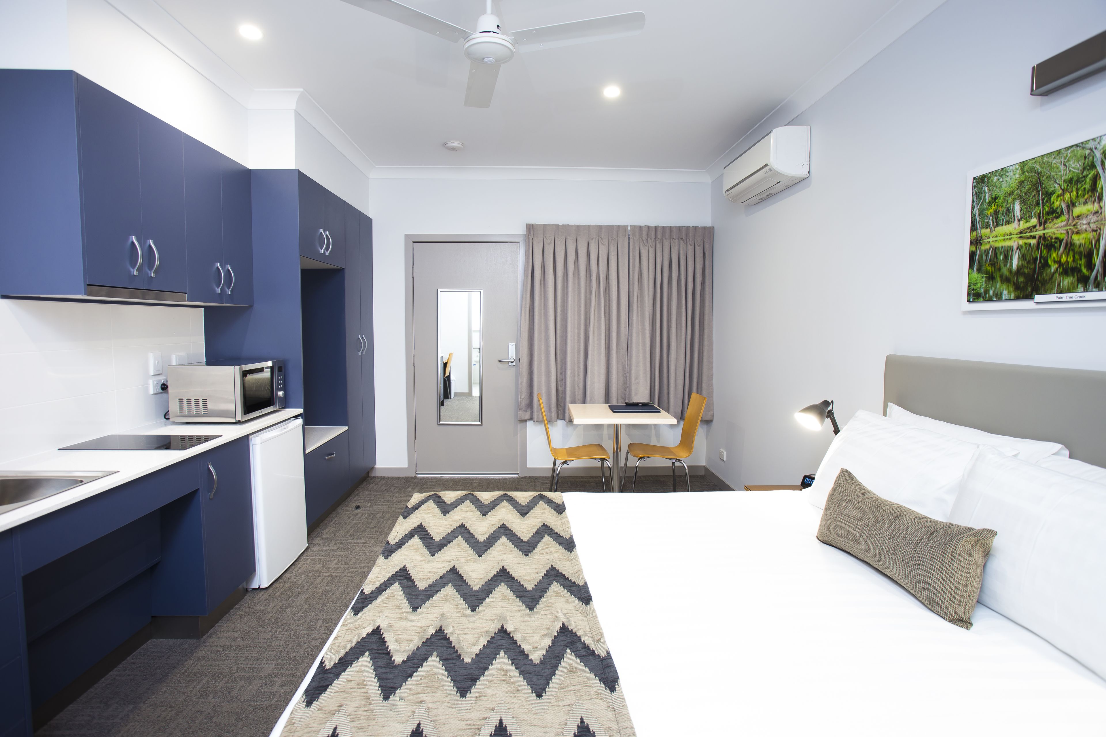 Ein modernes Hotelzimmer mit Bett, Schreibtisch, Sessel, Mikrowelle und Waschbecken.