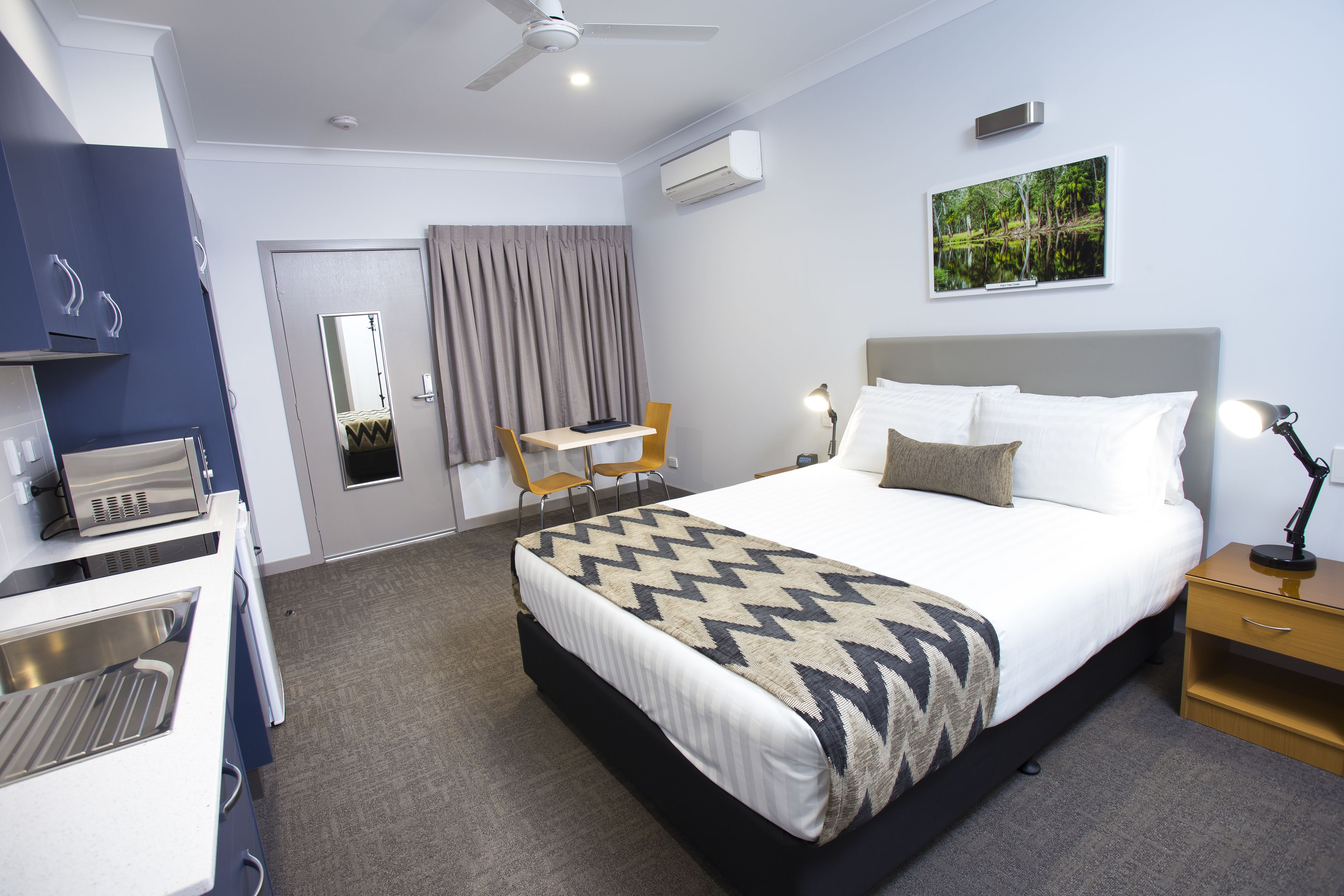 A hotel room with a bed, bedside table, lamp, and a desk with a chair.
