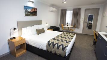 A hotel room with a bed, bedside table, lamp, and a view of the outside through the window.