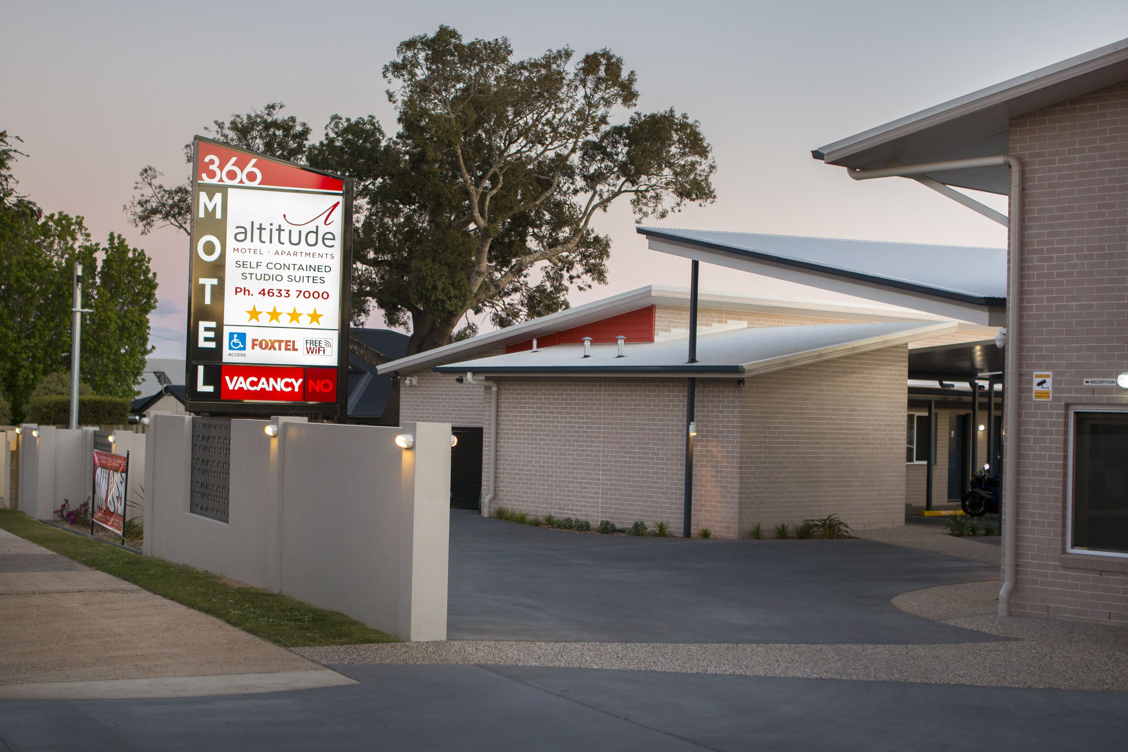 A motel sign with a vacancy notice, a modern building entrance, and a tree in the background.