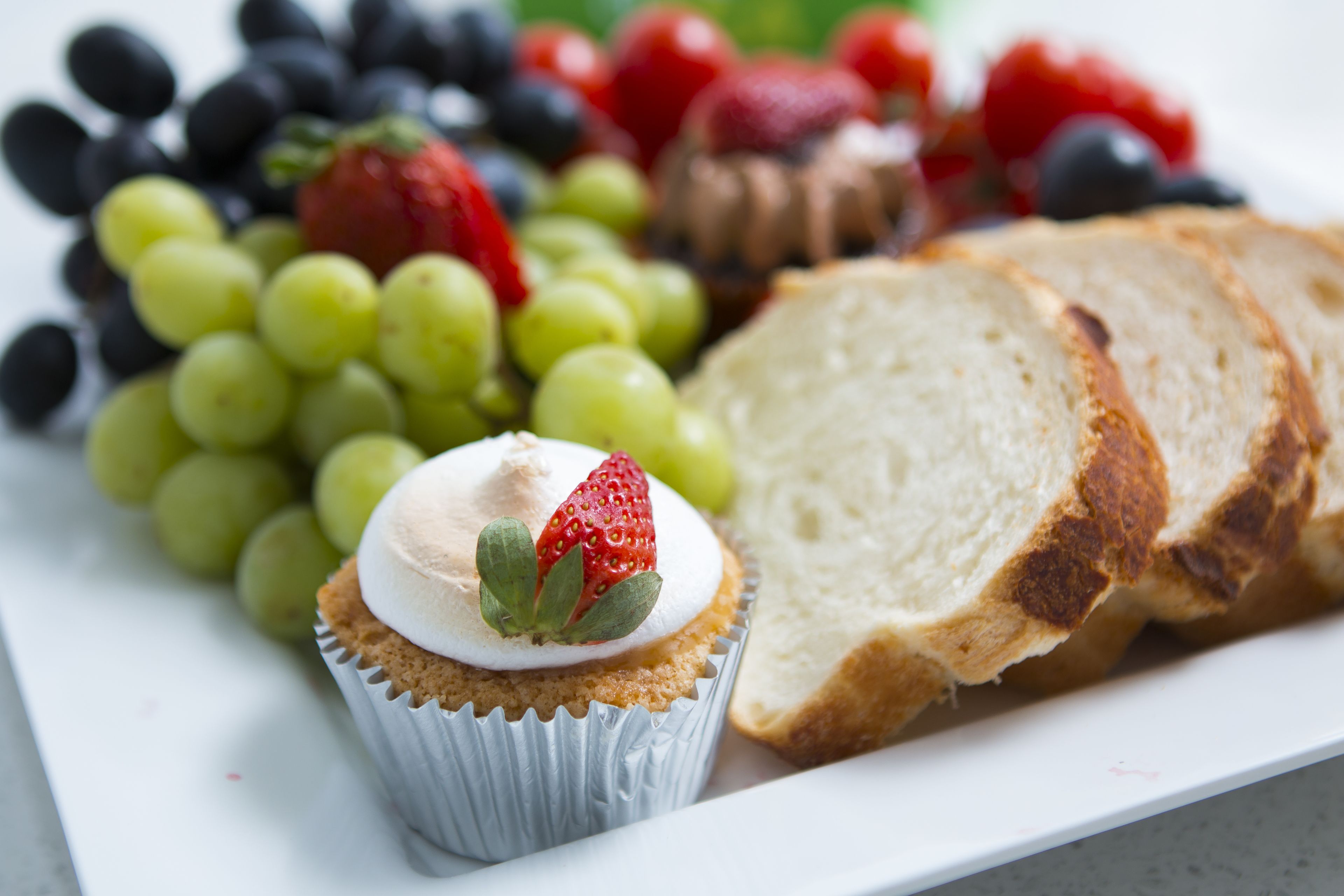 A plate with a cupcake, grapes, strawberries, and slices of bread.