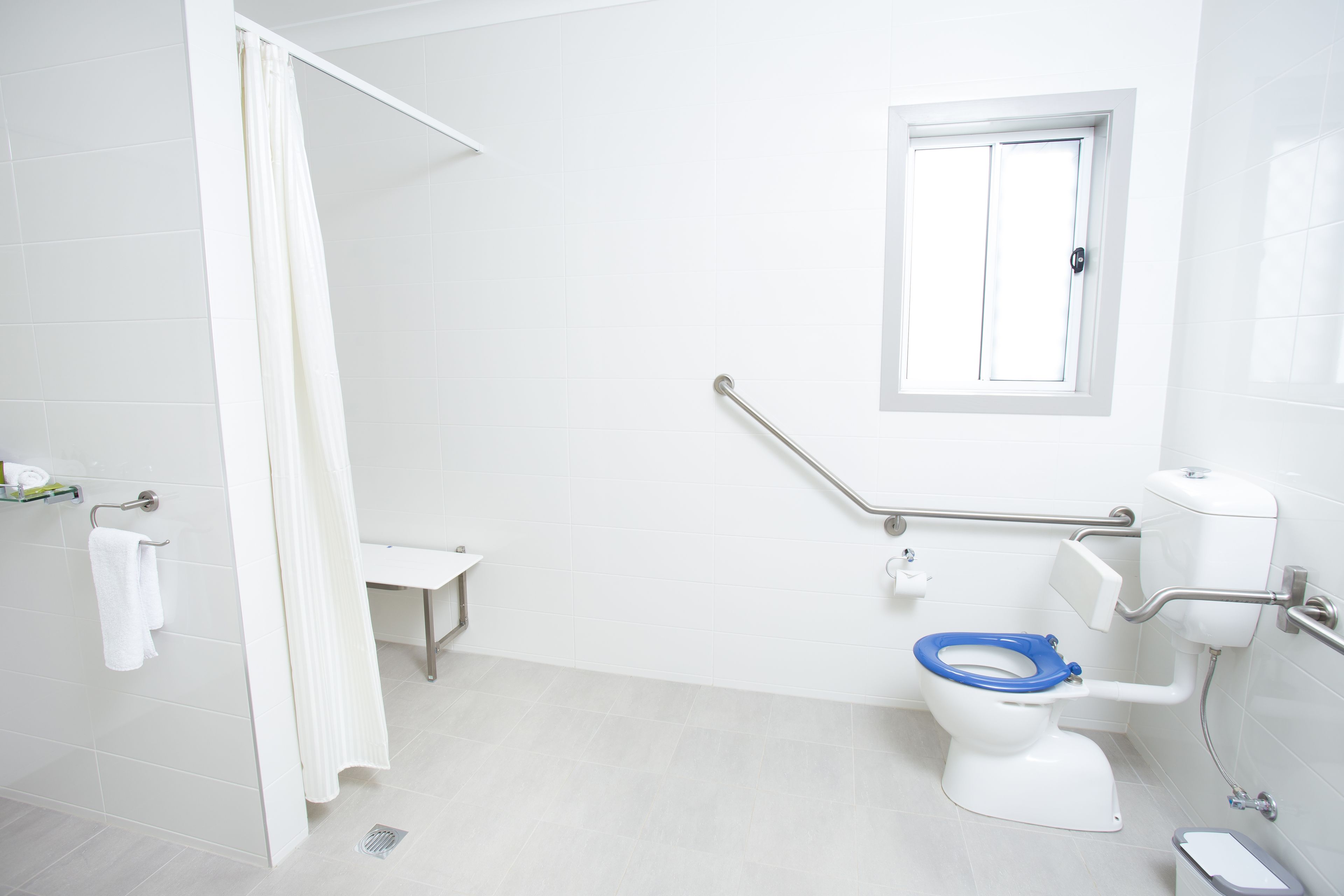A bathroom with a white toilet, a shower curtain, a window, and a grab bar.