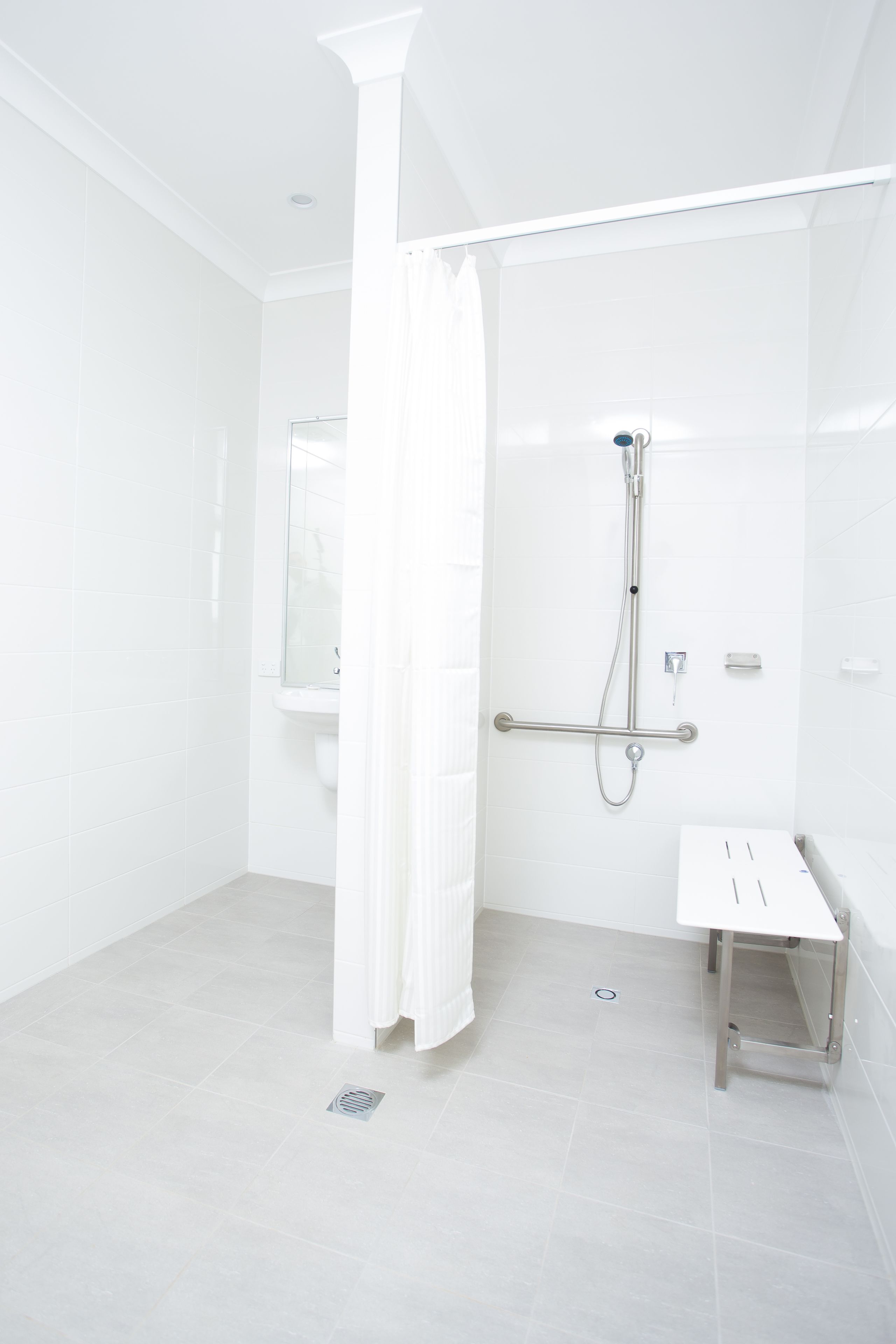 A modern bathroom with white tiles, a glass shower enclosure, a white sink, and a handheld showerhead.