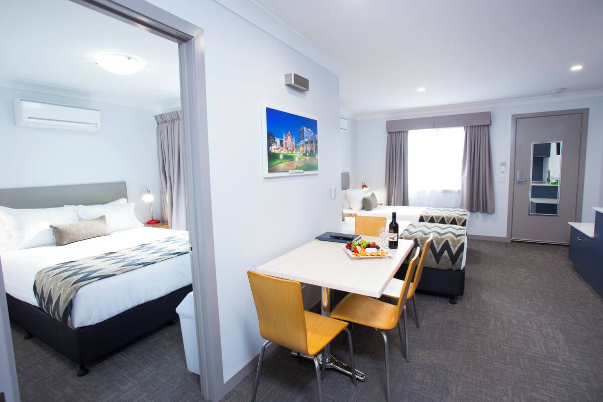 Ein Hotelzimmer mit Bett, Esstisch mit Stühlen, einer kleinen Küchenzeile und einem Badezimmer.