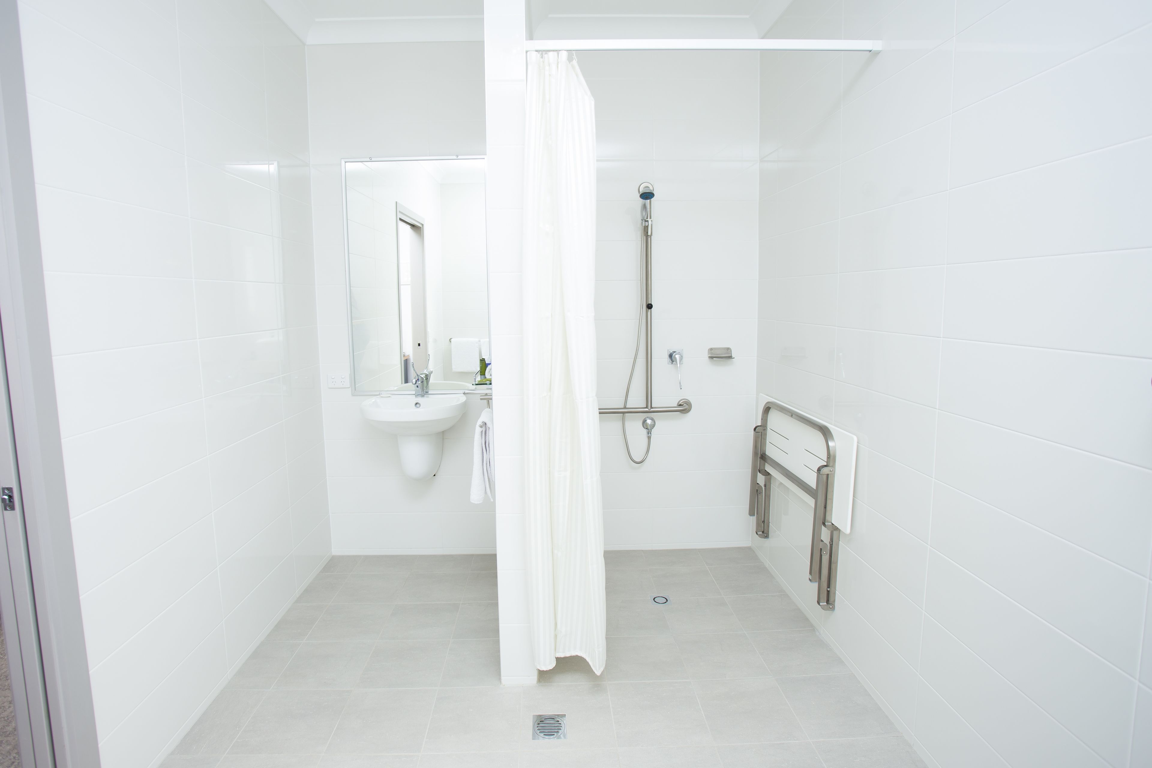 A small, white bathroom with a shower, a sink, and a mirror.