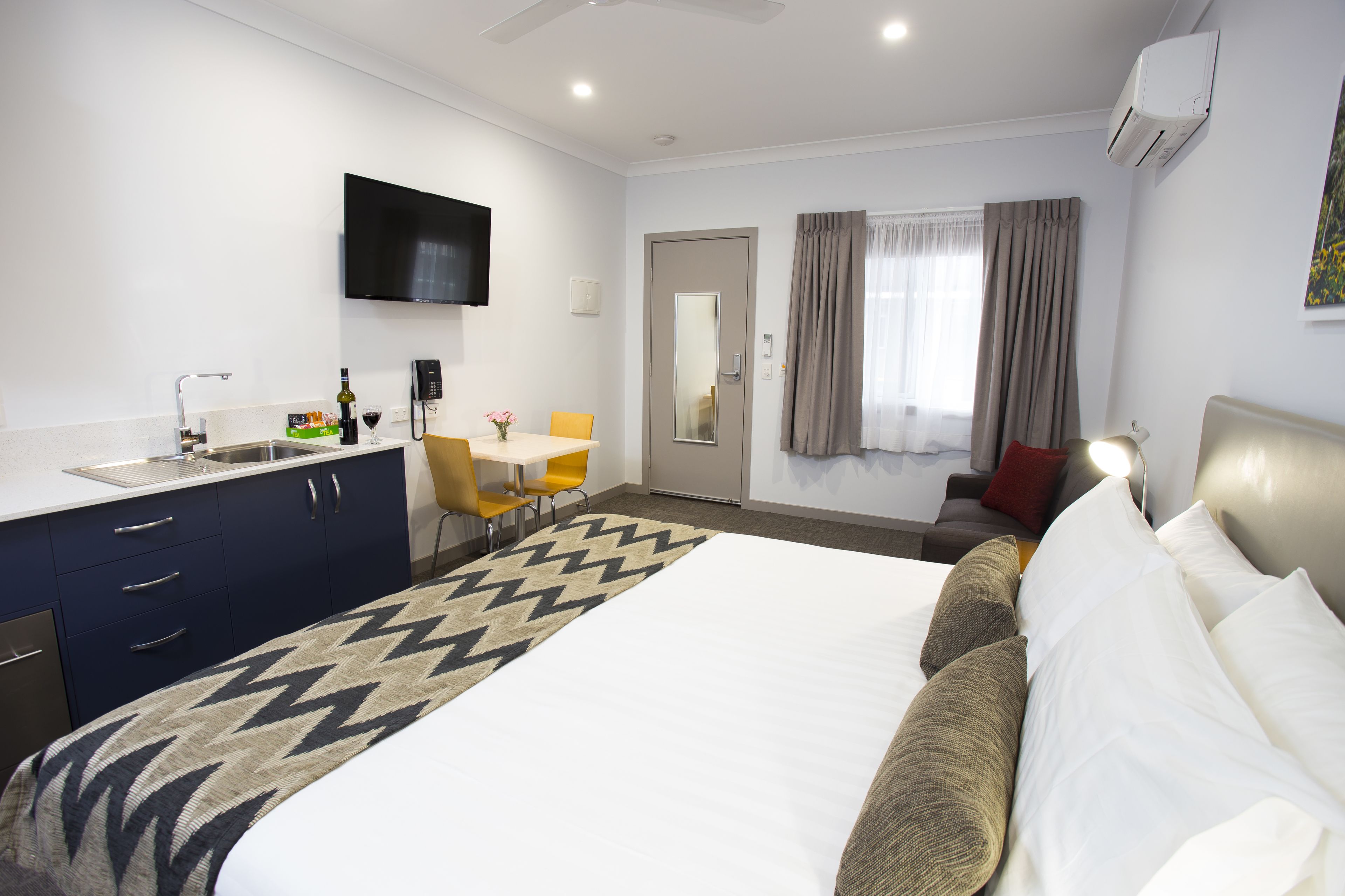 Une chambre d’hôtel avec un lit, un bureau, une chaise, une télévision et une fenêtre avec des rideaux.