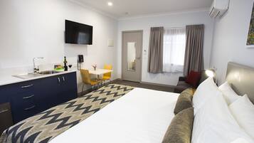 Une chambre d’hôtel avec un lit, un bureau, une chaise, une télévision et une fenêtre avec des rideaux.