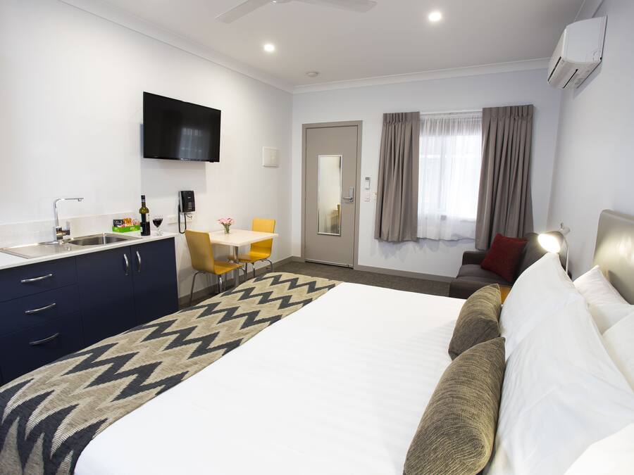 A hotel room with a bed, a desk, a chair, a TV, and a window with curtains.